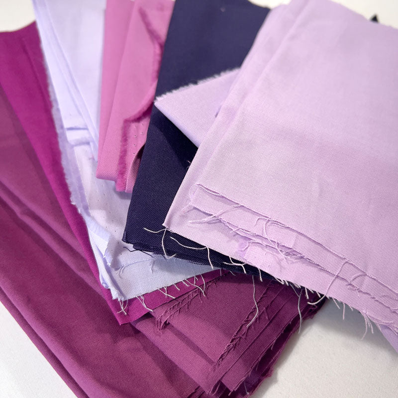 Stack of fabric swatches in various purple shades on a white background