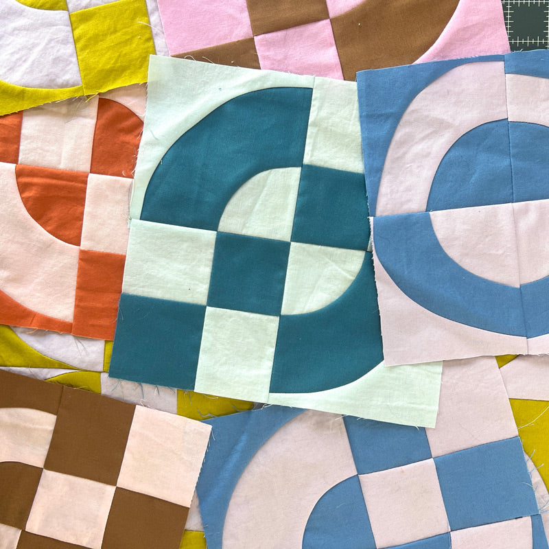 Quilt blocks in a pile, in multiple colors, made of 4 patches and drunkards path blocks