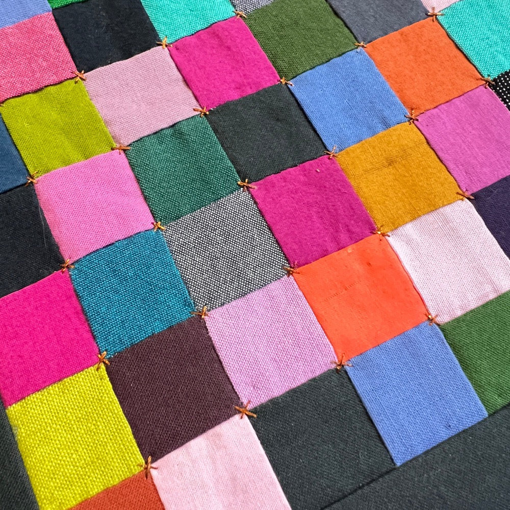 Close up Small hand sewn quilt of bright colored squares, finished with embroidery in bronze thread.